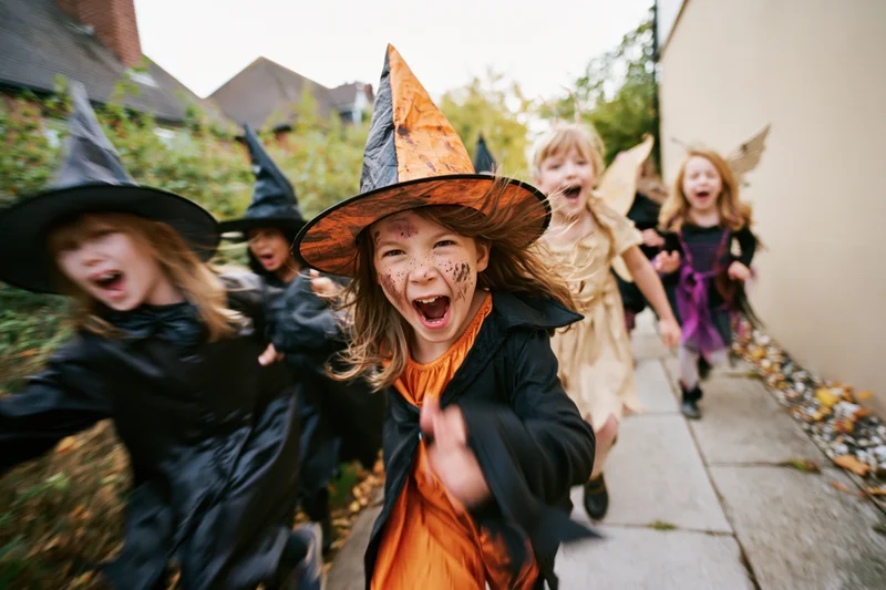 Children in halloween costumes running excitedly down a sidewalk