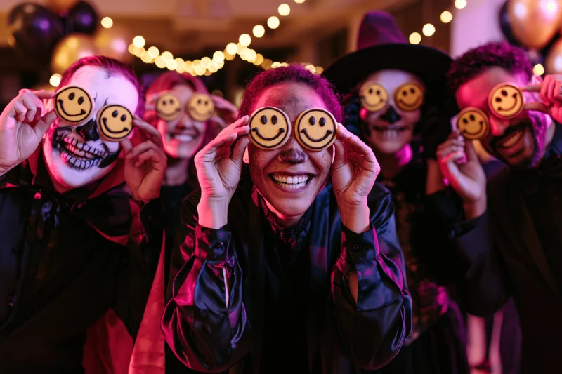 Group of adults in halloween costumes holding smiley cookies over their eyes at a festive party