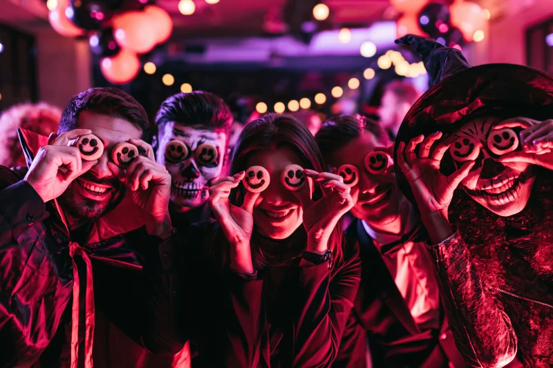 Five adults in halloween costumes holding smiley cookies over their eyes at a party