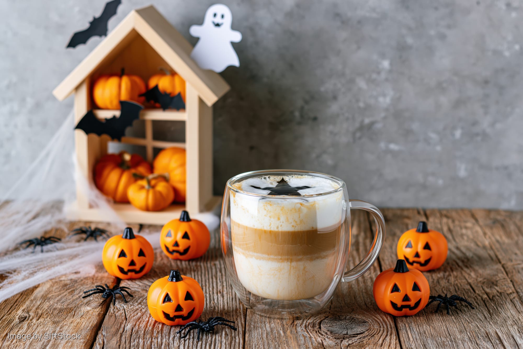 Halloween-themed coffee latte with pumpkin decorations on a rustic wooden table