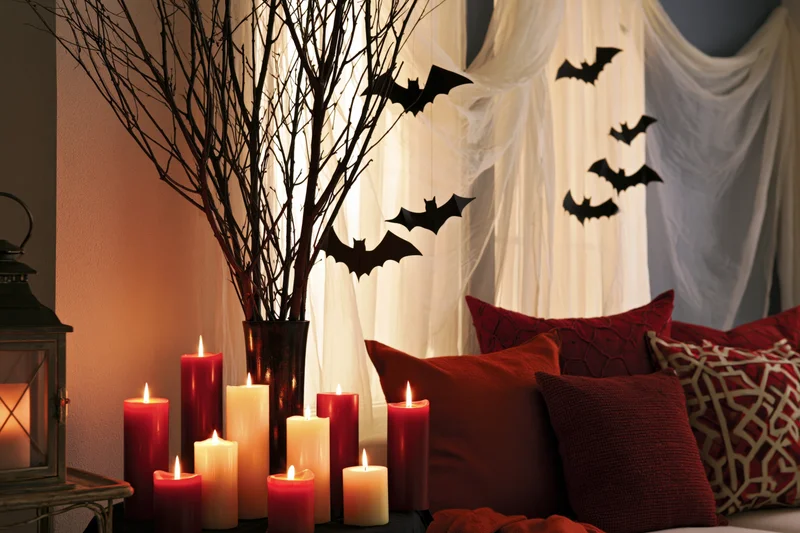 Halloween decorated corner with lit candles, bare branches in vase, and bat silhouettes on draped fabric behind red pillows