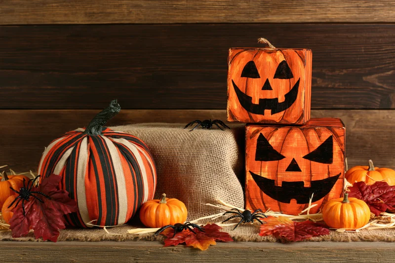 Halloween decorations including carved wooden pumpkins, fabric pumpkins, spiders, and autumn leaves arranged on a rustic wooden surface