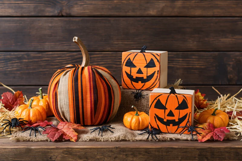 Halloween decorations including fabric pumpkins and wooden jack-o-lanterns arranged on a rustic wooden table with hay and autumn leaves