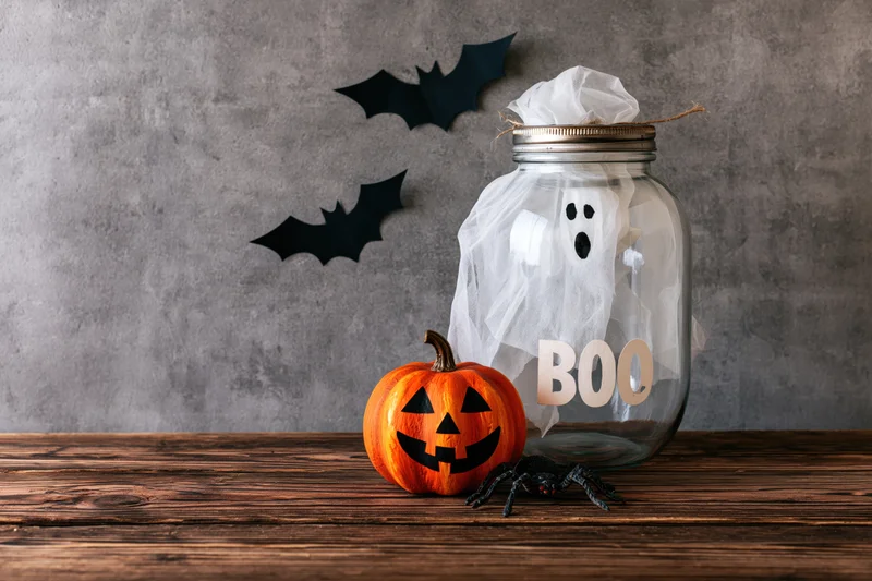 Halloween decorations including a carved pumpkin, ghost in a jar, and paper bats arranged on a rustic wooden table