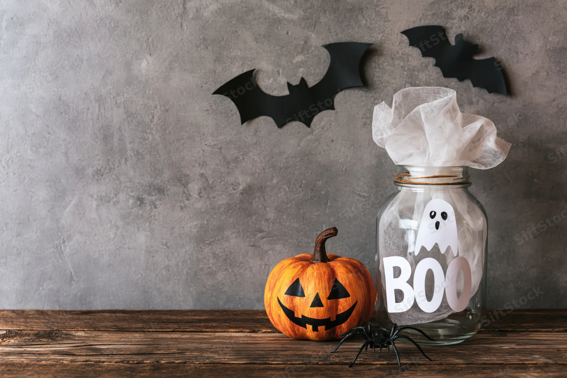 Halloween decorations including a jackolantern, ghost in a jar, and bats on a rustic wooden table