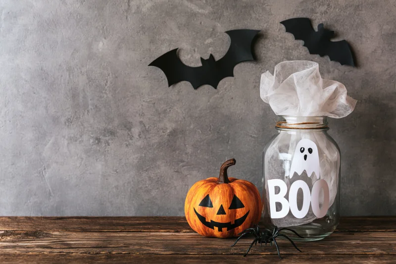 Halloween decorations including a jackolantern, ghost in a jar, and bats on a rustic wooden table