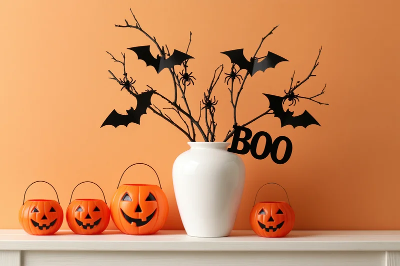 Halloween decorations including pumpkins, bats, and branches in a white vase arranged on a white shelf against an orange wall