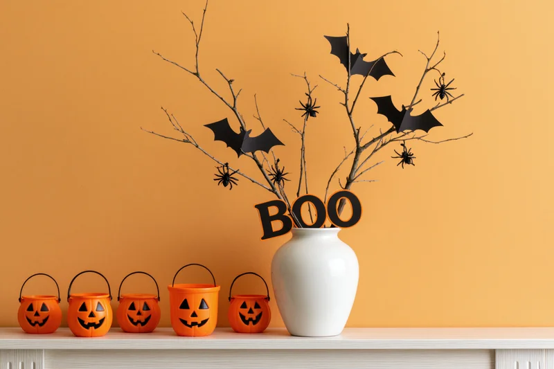 Halloween decorations including pumpkins and bats arranged on a white shelf against an orange wall