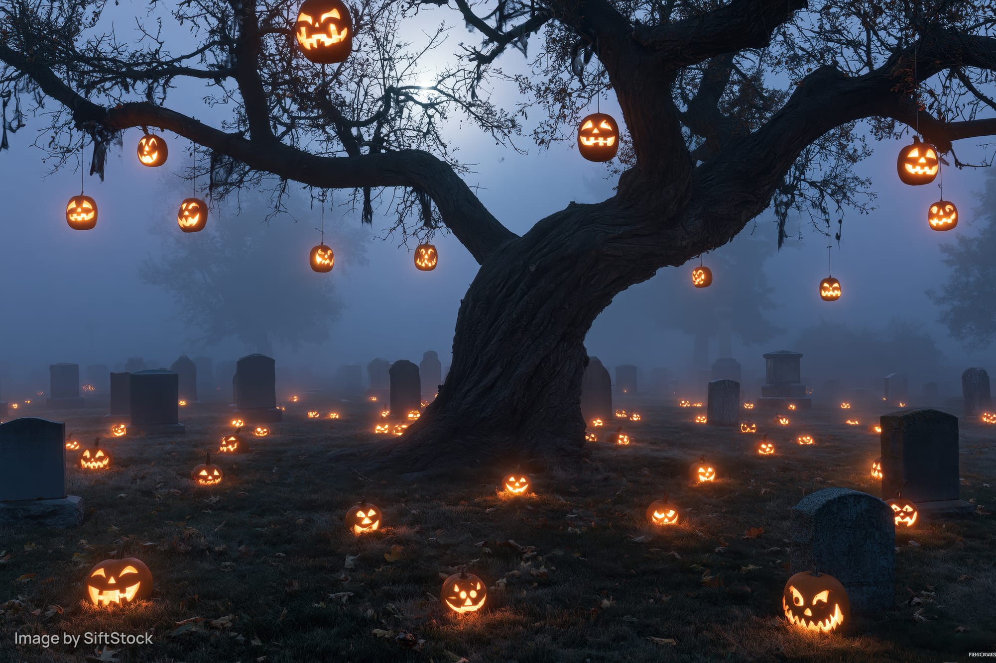 Carved jack-o-lanterns hanging from a gnarled tree and scattered across a foggy graveyard at night