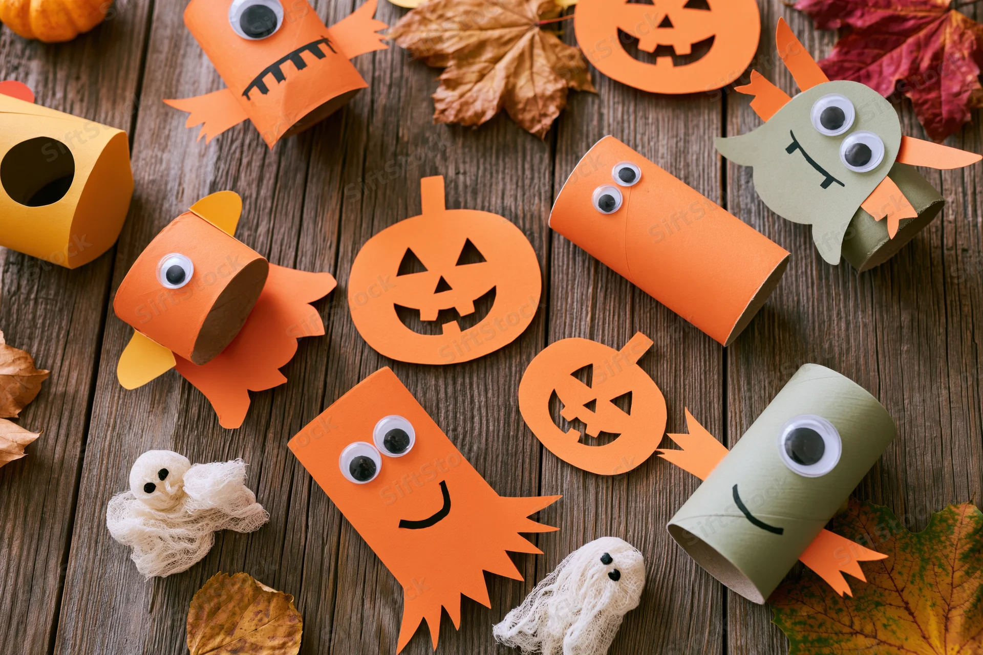 Halloween kids craft project flat lay on rustic wooden table with paper pumpkins ghosts and leaves