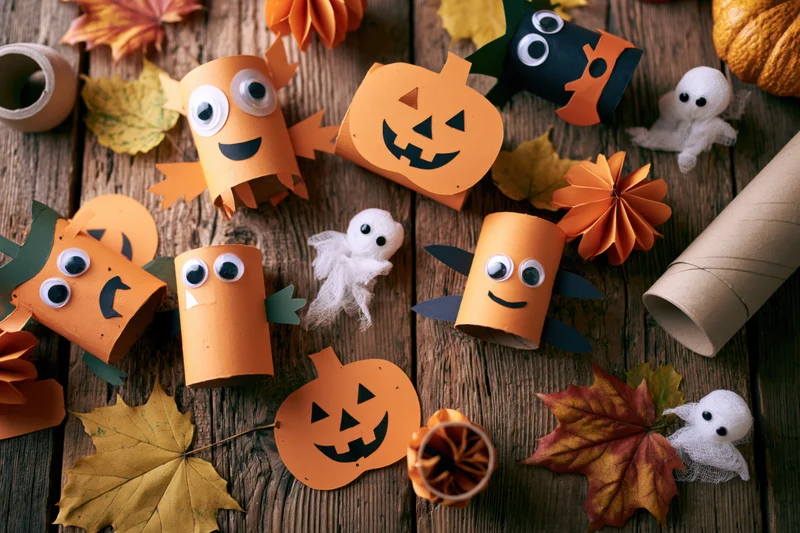 Halloween kids craft project flat lay on rustic wooden table with paper pumpkins ghosts and autumn leaves