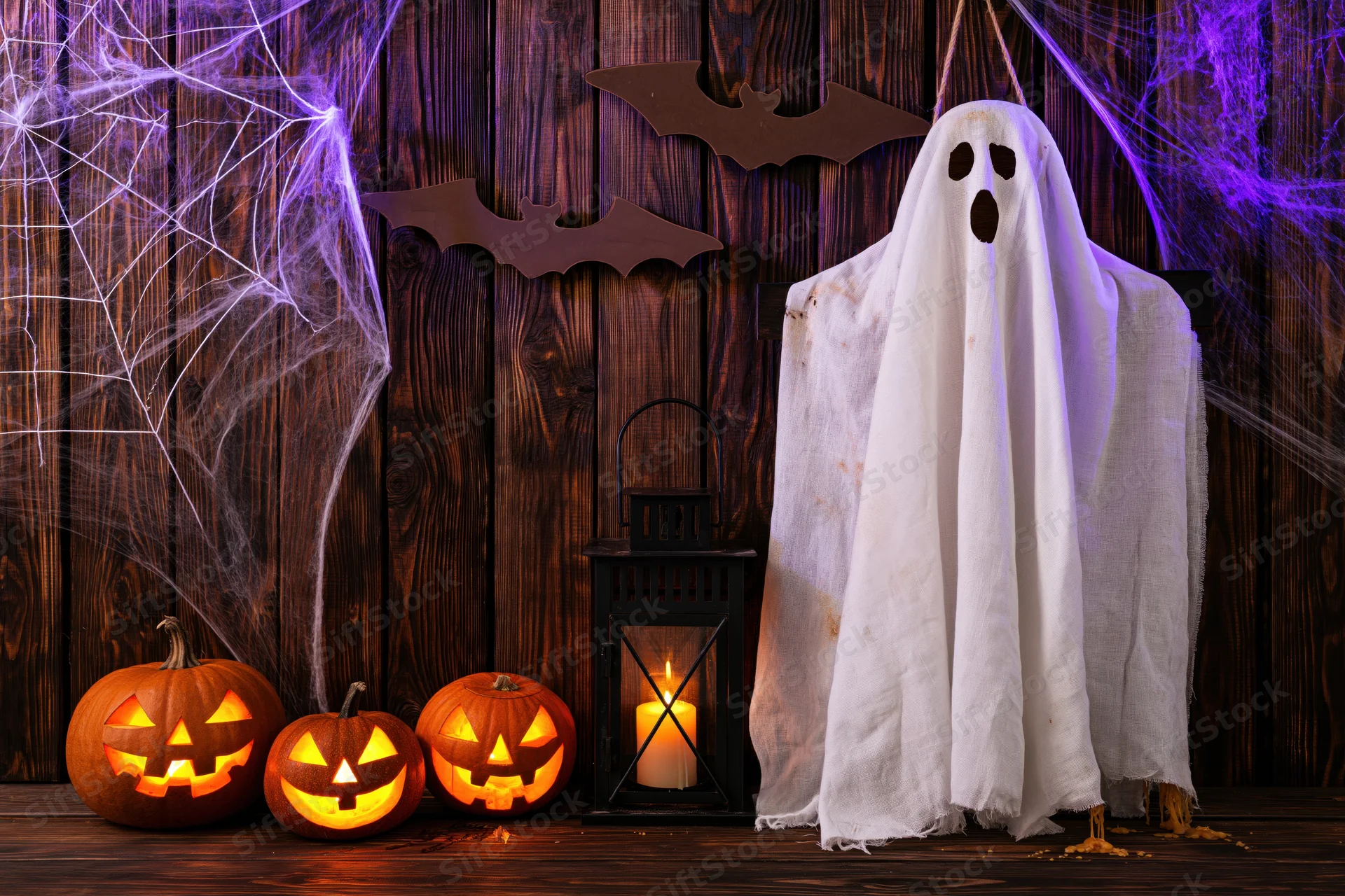 Hanging white fabric ghost with carved pumpkins and lantern on a wooden porch decorated for halloween