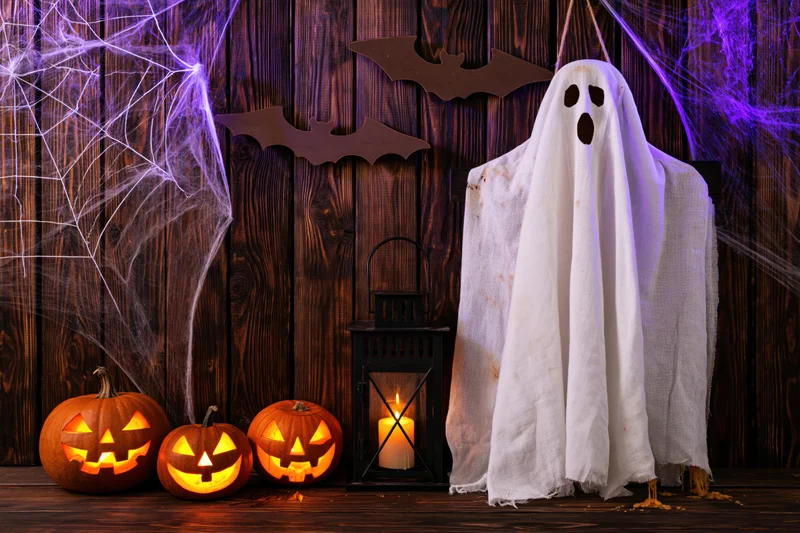 Hanging white fabric ghost with carved pumpkins and lantern on a wooden porch decorated for halloween