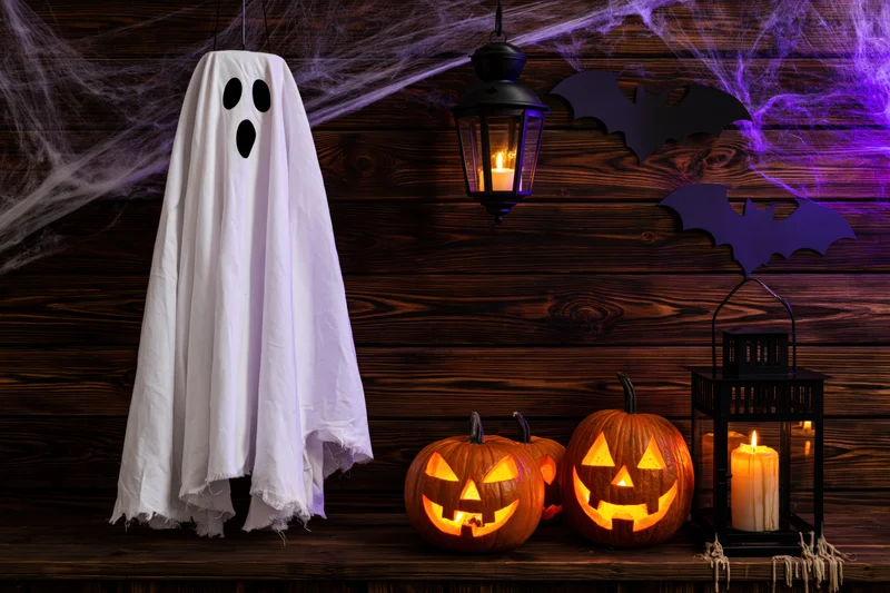 Hanging white fabric ghost with carved pumpkins and lanterns on a wooden porch decorated for halloween