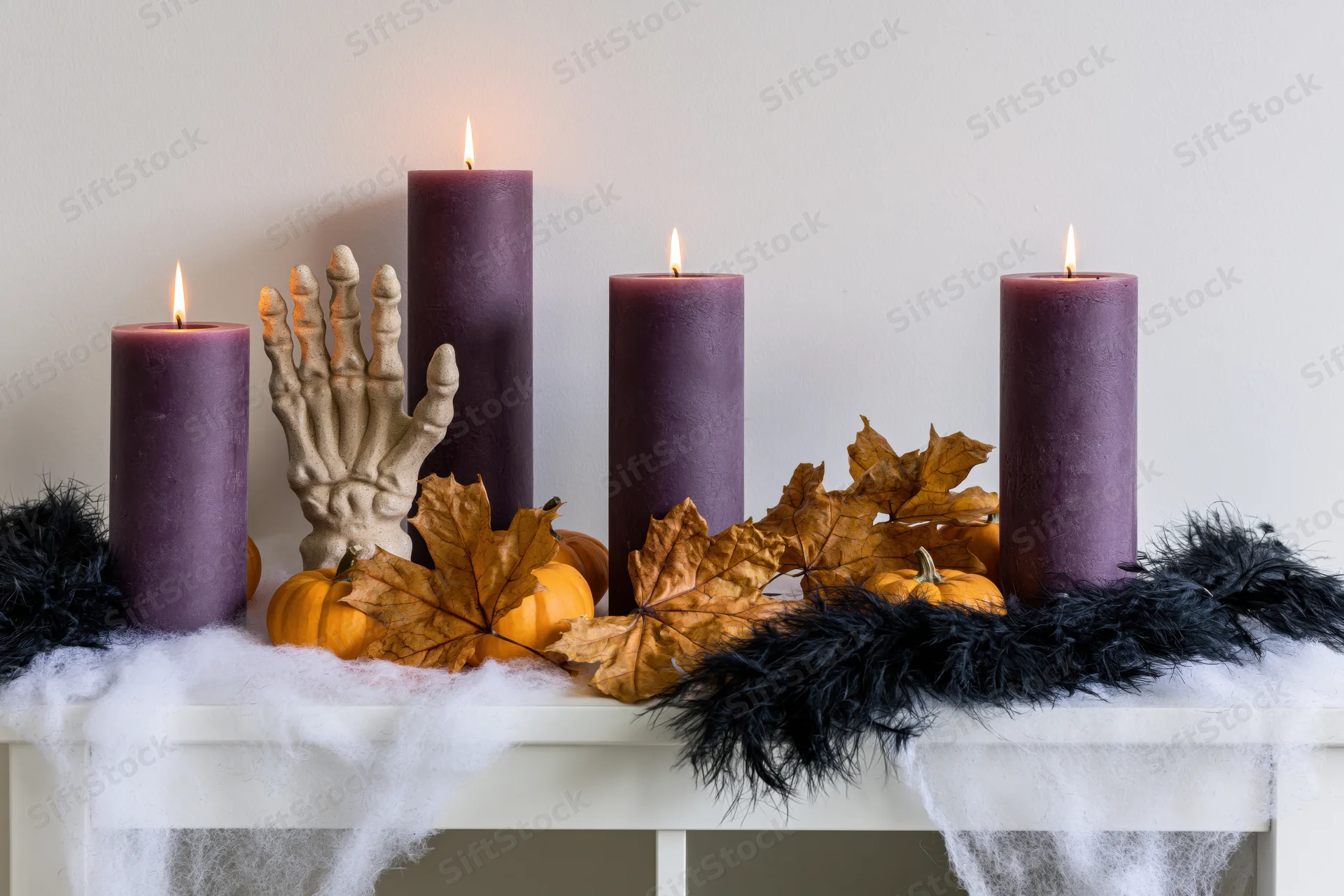 Halloween shelf display with lit purple candles, pumpkins, autumn leaves, skeleton hand, and cobwebs