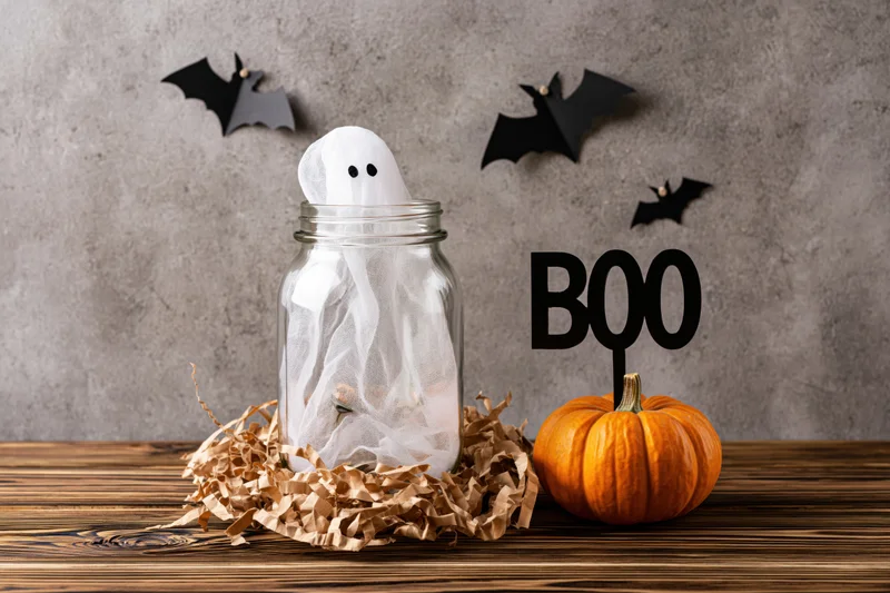 Halloween decoration with ghost in mason jar and pumpkin on wooden table