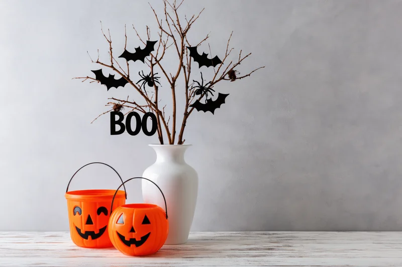 Halloween decoration with jack-o-lantern buckets and a vase of branches with bats and spiders on a wooden table