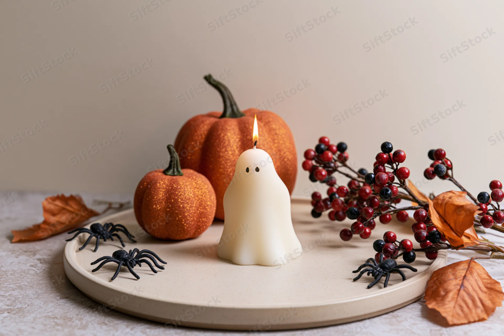 Ghost-shaped candle lit on a tray with pumpkins, spiders, berries and leaves for halloween decoration
