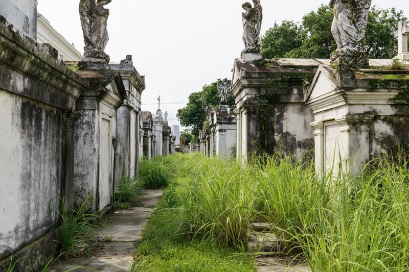 Row of historic aboveground mausoleums with angel statues along a grassy pathway in a cemetery