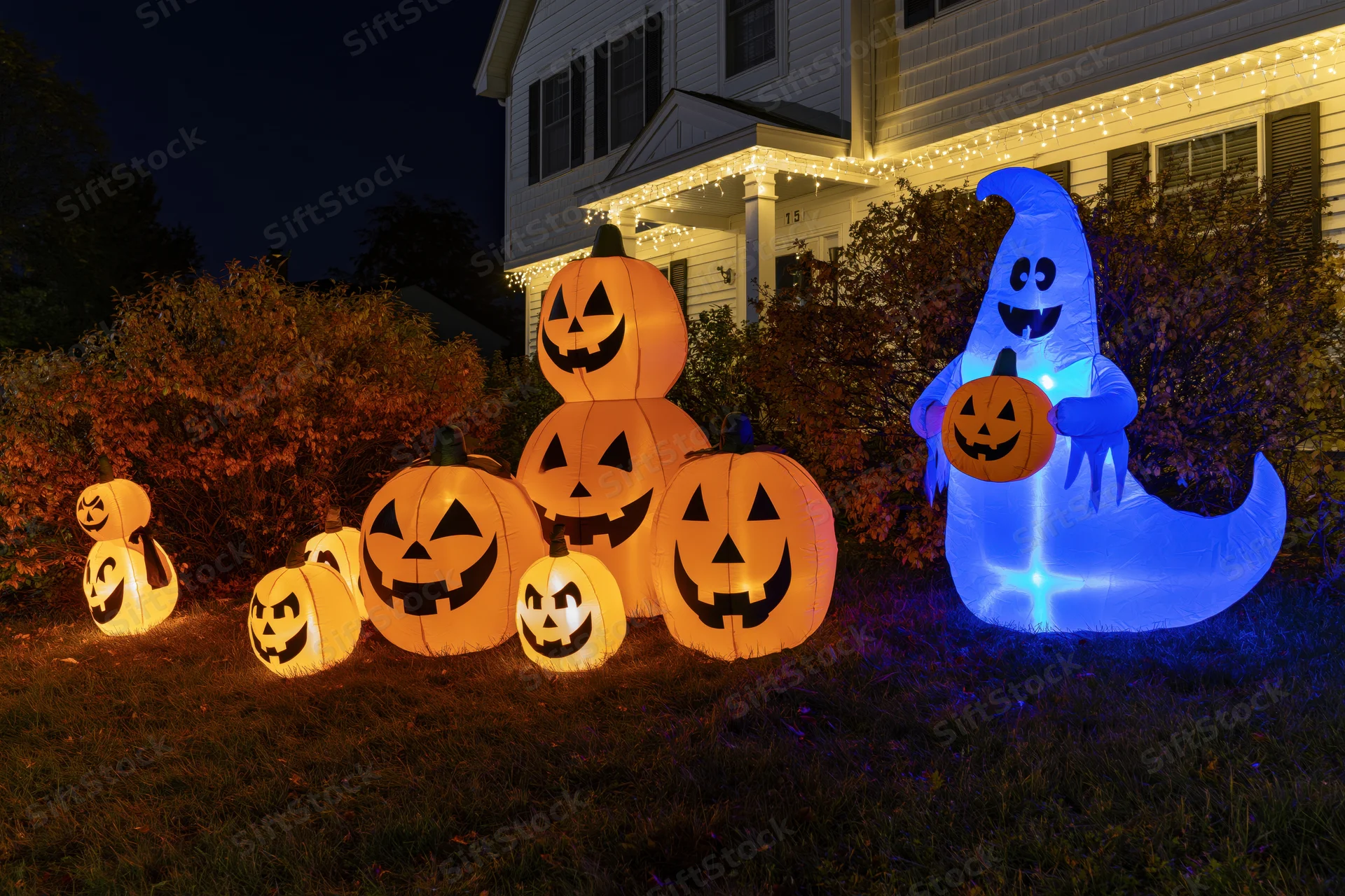 Inflatable halloween pumpkins and ghost glowing on front lawn at night