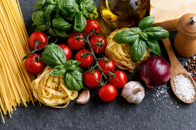 Italian cooking ingredients arranged along the bottom edge of a dark slate surface