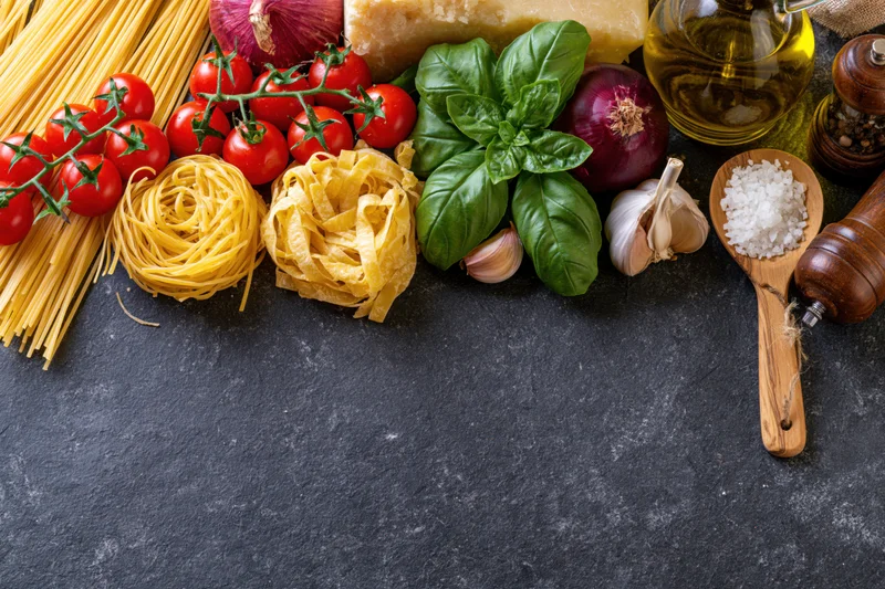 Italian cooking ingredients arranged along the bottom edge of a dark countertop with copyspace above