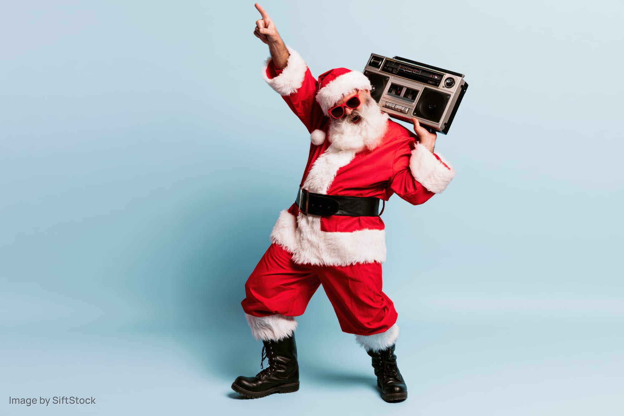 Man dressed as santa claus dancing with boombox and pointing upward against blue background