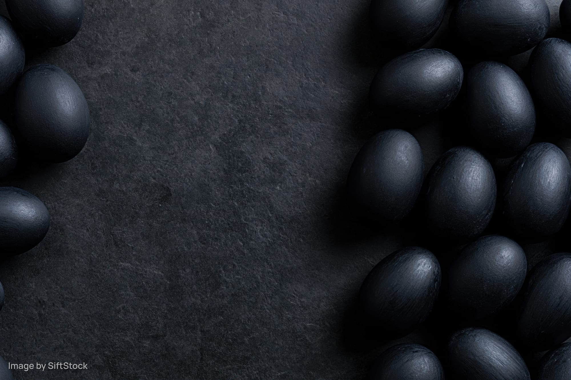 Matte black painted eggs arranged along the left and right edges on a dark stone surface with central copyspace