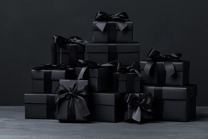 Stacked black gift boxes with ribbons arranged on a dark surface
