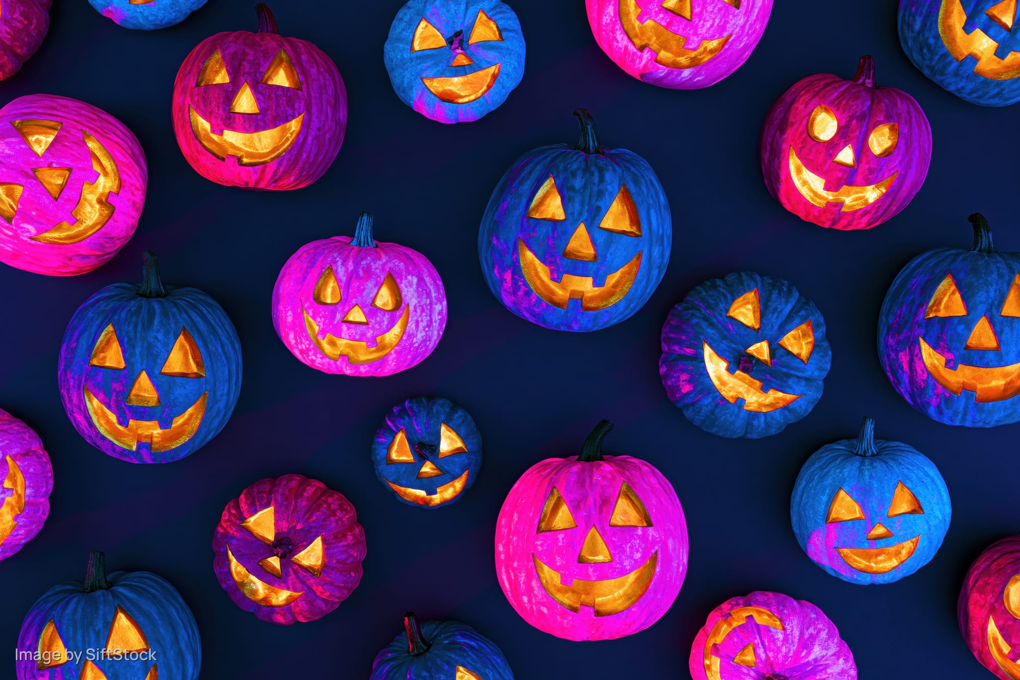 Colorful carved jack-o-lantern pumpkins arranged in a flat lay pattern on dark background
