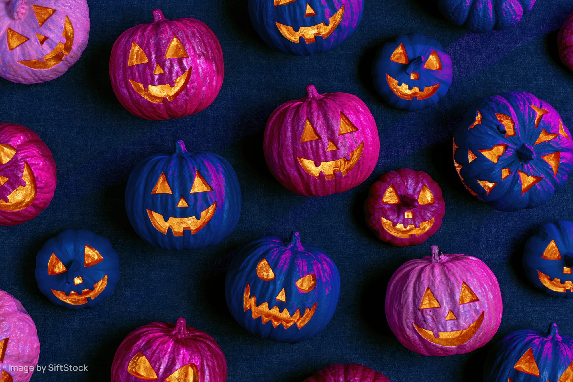 Carved jack-o-lantern pumpkins in purple and blue arranged on dark fabric surface