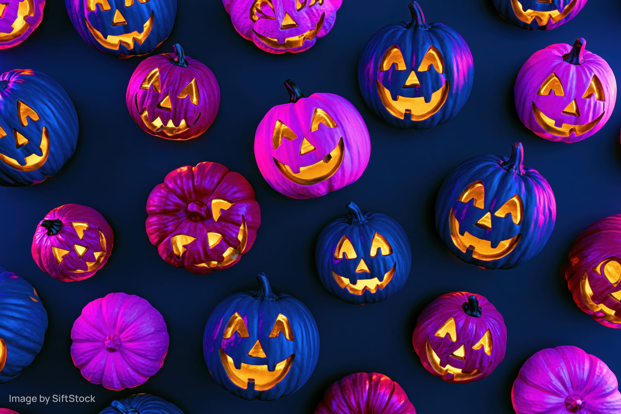 Carved jack-o-lantern pumpkins glowing in purple and blue arranged in a flat lay pattern on dark background