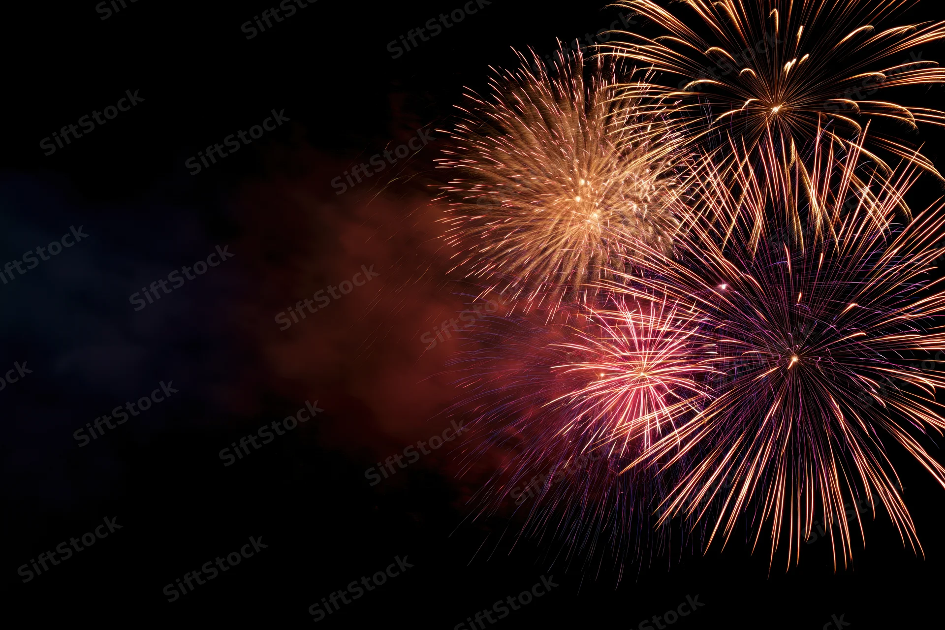Fireworks bursting in the night sky with trails of golden and pink light against a dark background