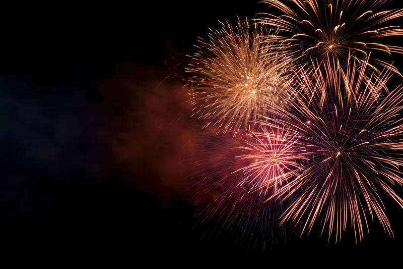 Fireworks bursting in the night sky with trails of golden and pink light against a dark background