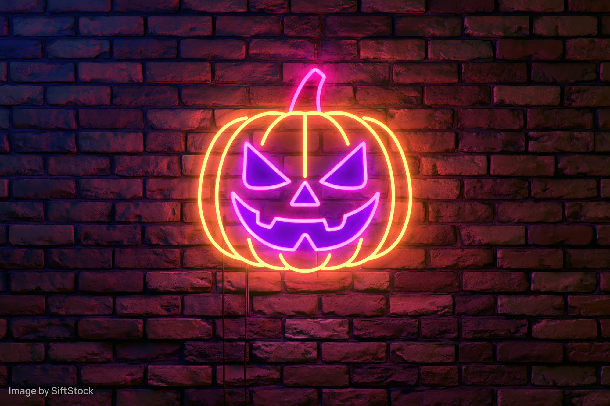 Neon jack-o-lantern sign glowing on dark brick wall