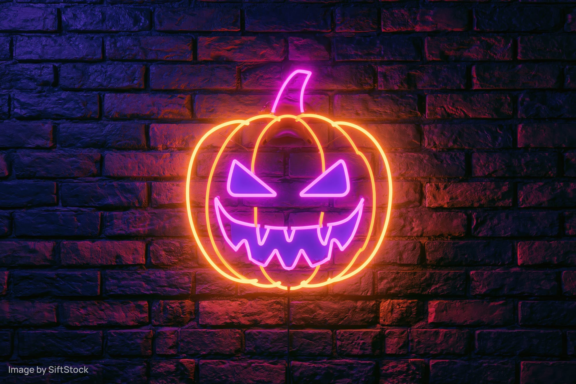 Neon jack-o-lantern sign glowing on dark brick wall