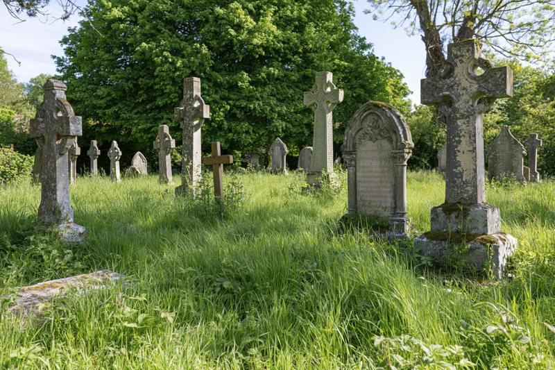 Weathered stone crosses and tombstones in a grassy british cemetery surrounded by trees