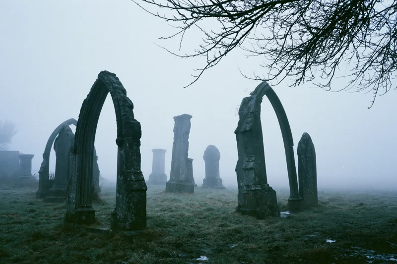 Weathered stone arches and tombstones in a foggy old english cemetery on a misty morning