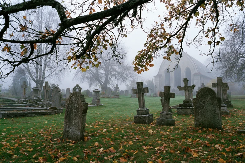 Foggy autumn morning in an old european cemetery with stone tombstones and a church in the background
