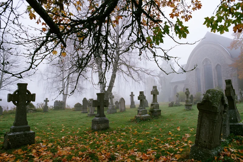 Foggy autumn morning in an old european cemetery with stone graves and a church in the background