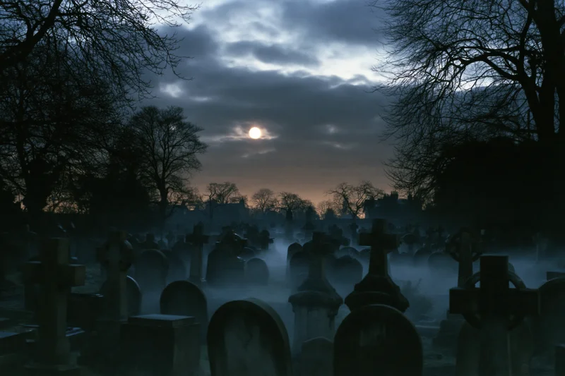 Rows of weathered gravestones in a foggy cemetery at night under a full moon