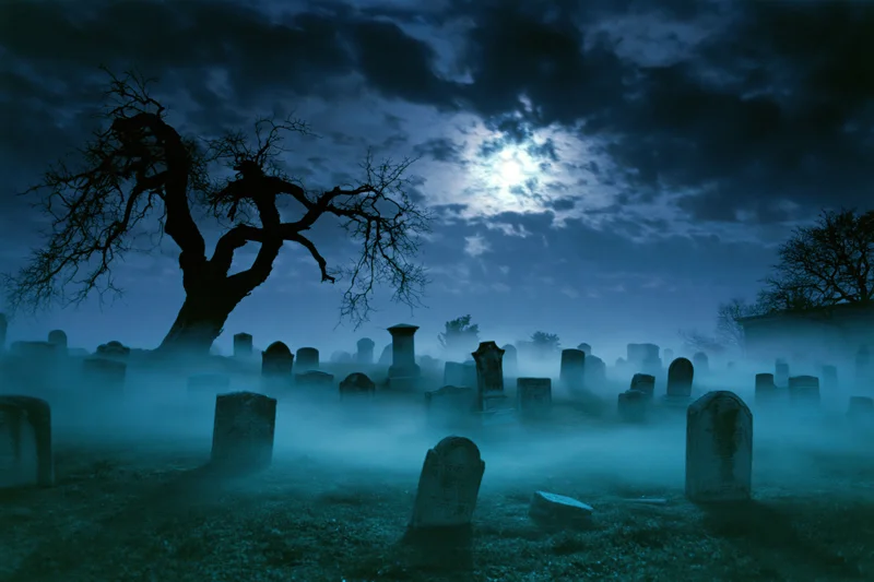 Foggy old cemetery at night with weathered gravestones and bare trees under a full moon