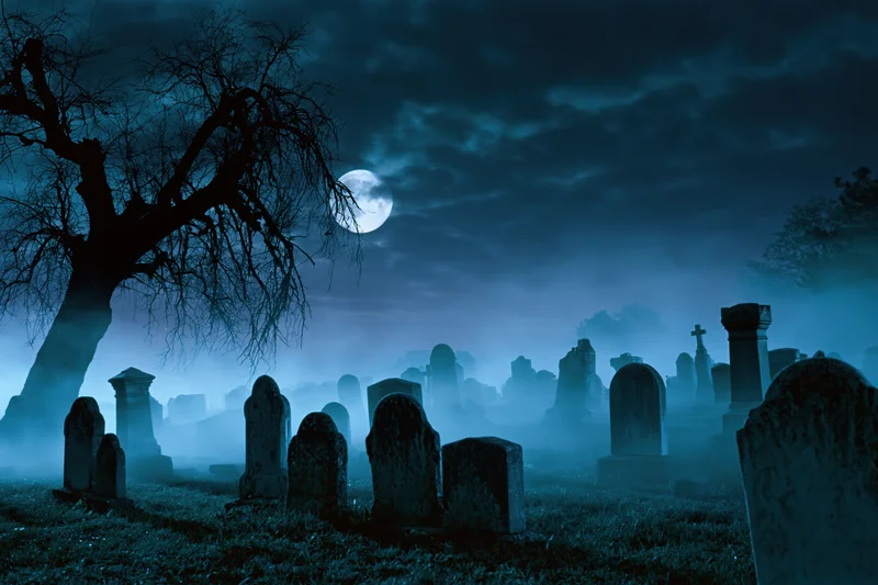 Old cemetery at night with weathered gravestones and bare trees under a full moon in fog