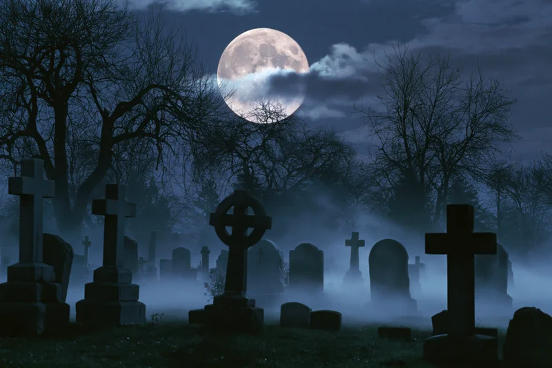 Old cemetery at night with stone crosses and tombstones under a full moon, surrounded by fog and bare trees