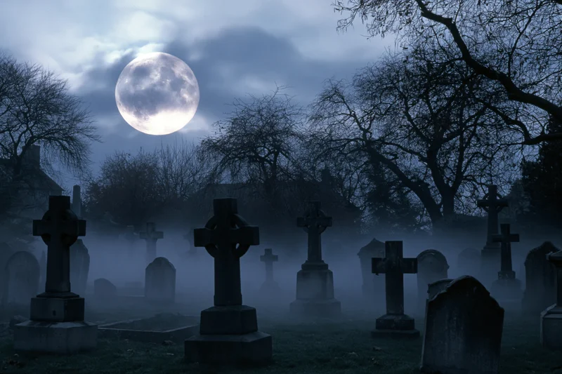 Foggy old cemetery at night with stone crosses and tombstones under a full moon