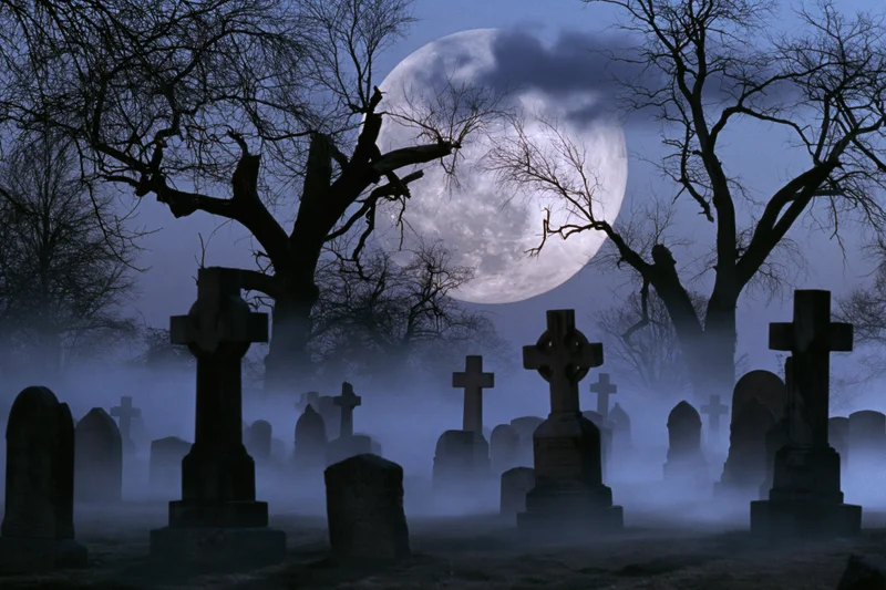 Foggy old cemetery at night with stone crosses and bare trees under a full moon