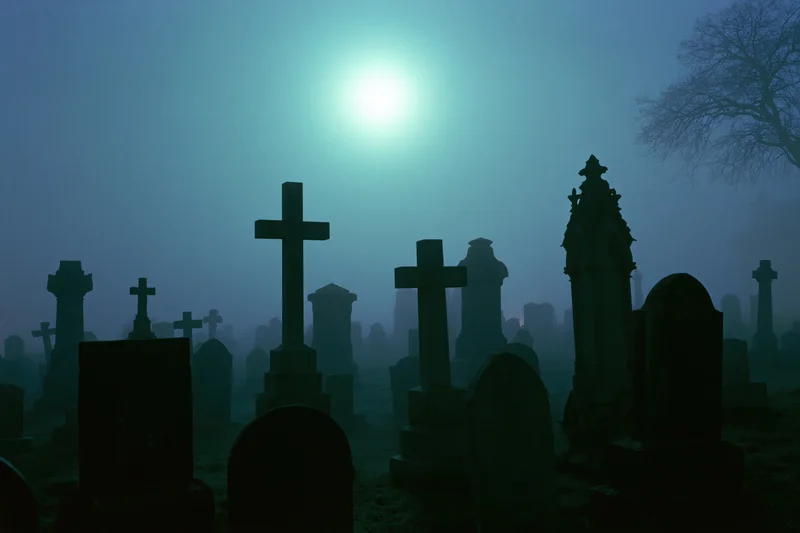 Silhouetted gravestones and crosses in a foggy cemetery at night under moonlight