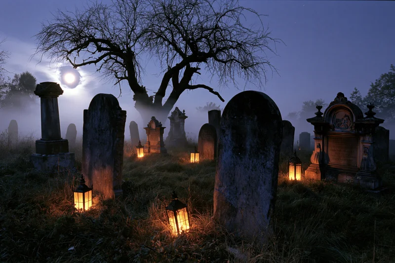 Old cemetery at night with weathered stone gravestones and glowing lanterns under a full moon, surrounded by fog and bare trees