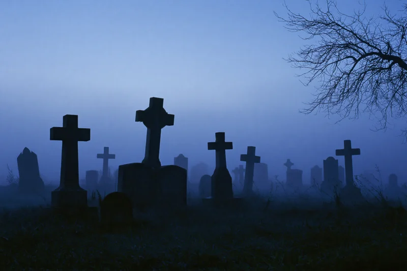 Silhouetted stone crosses and grave markers in a misty old cemetery at twilight