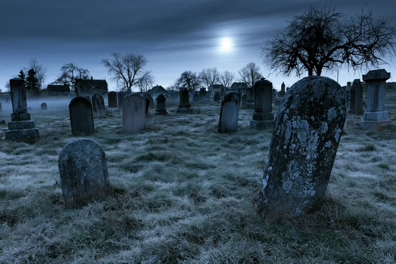 Old rural cemetery at night with weathered stone tombstones under a full moon and frosty grass